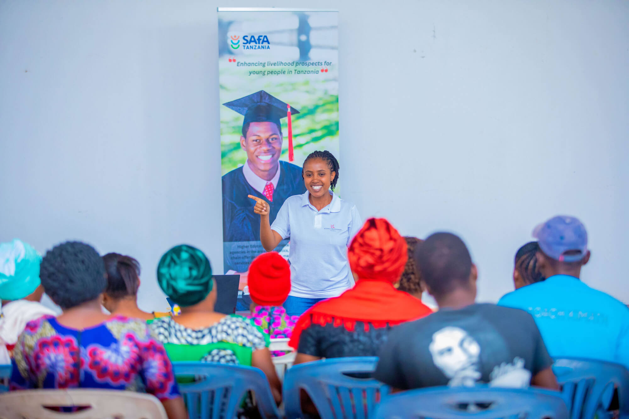 A woman speaks to an audience seated in front of a banner for SAFA Tanzania, promoting youth livelihood prospects.