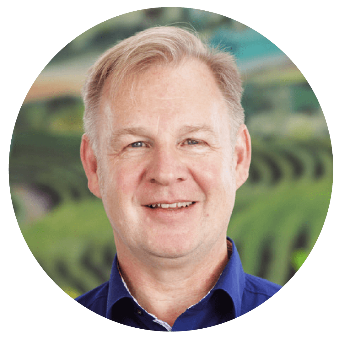 A smiling man with short hair, wearing a blue shirt, is shown against a blurred green background.