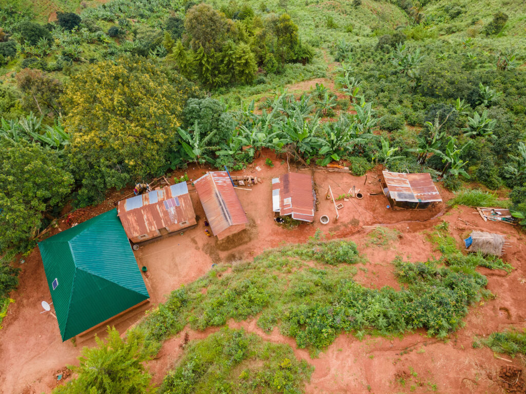 Aerial view of a rural homestead with several buildings surrounded by lush greenery and crops on a red dirt landscape.