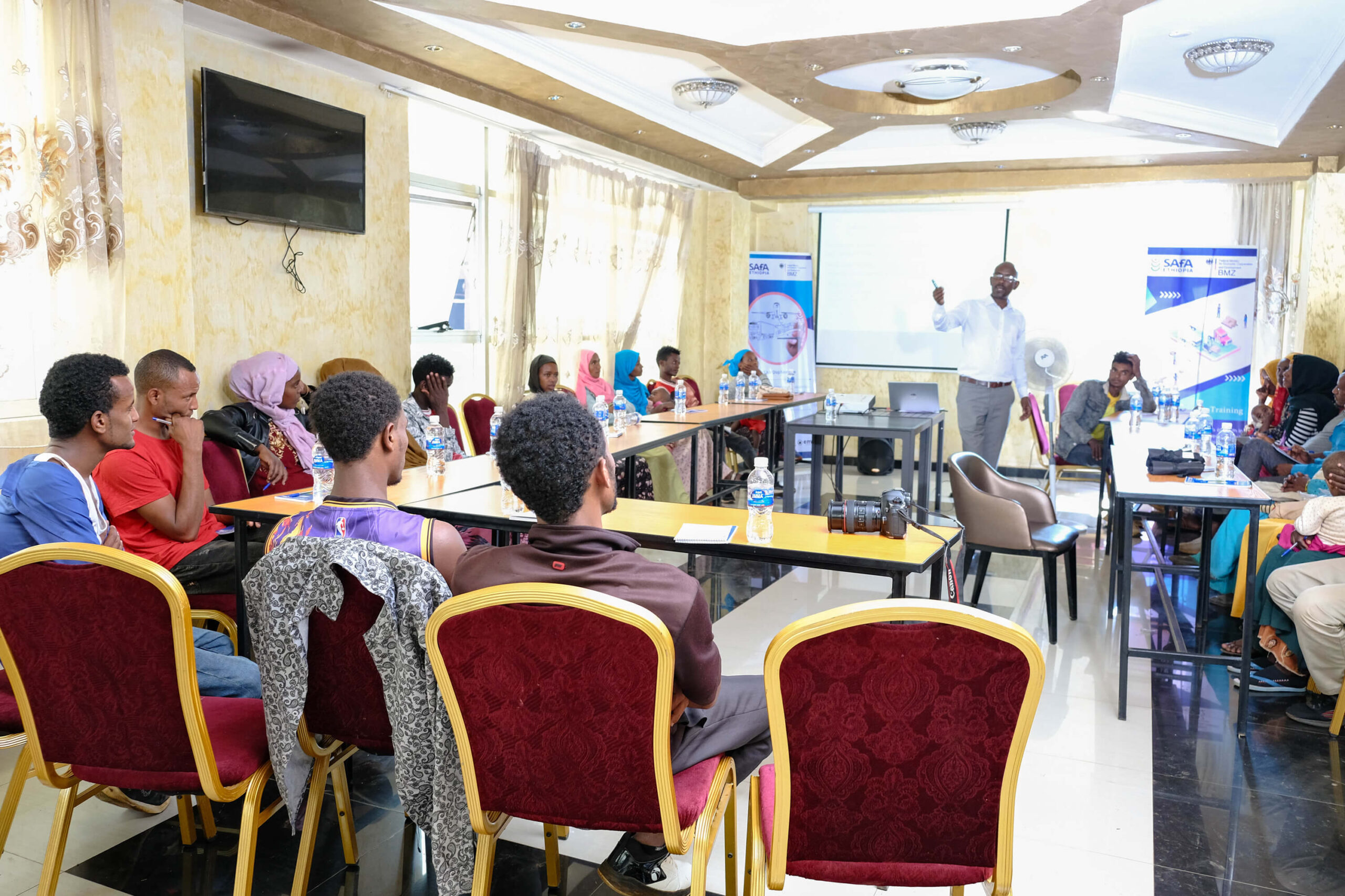 A group of people attends a training session in a conference room, with a speaker presenting in front.