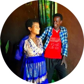 A man and a woman are smiling together in a dimly lit room, with green curtains and a warm, friendly atmosphere.