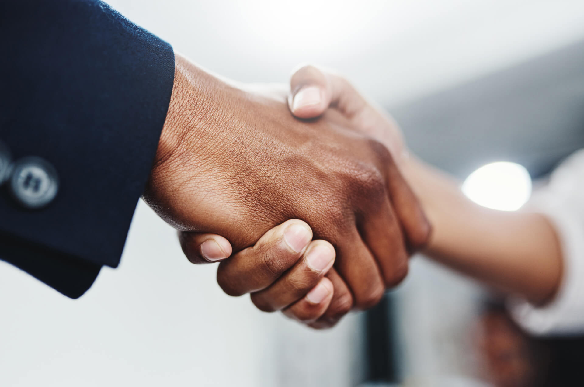 Two hands engaged in a handshake, one wearing a dark suit jacket, conveying a sense of agreement or partnership.