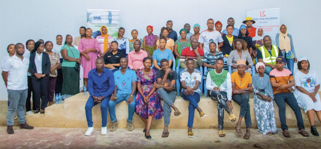 A diverse group of individuals poses for a photo, with banners from SAFa and a foundation in the background.